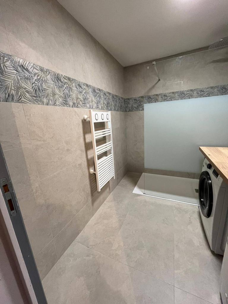 Zone douche rénovée avec paroi, carrelage et finitions sanitaires